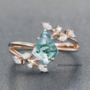 Könnte beinhalten: Ein roségoldener Ring mit einem rautenförmigen Moosachat-Edelstein mit grünen Adern. Der Ring ist mit kleinen, klaren Edelsteinen und zarten, astähnlichen Details verziert. Der Ring hat ein geteiltes Schaftdesign.