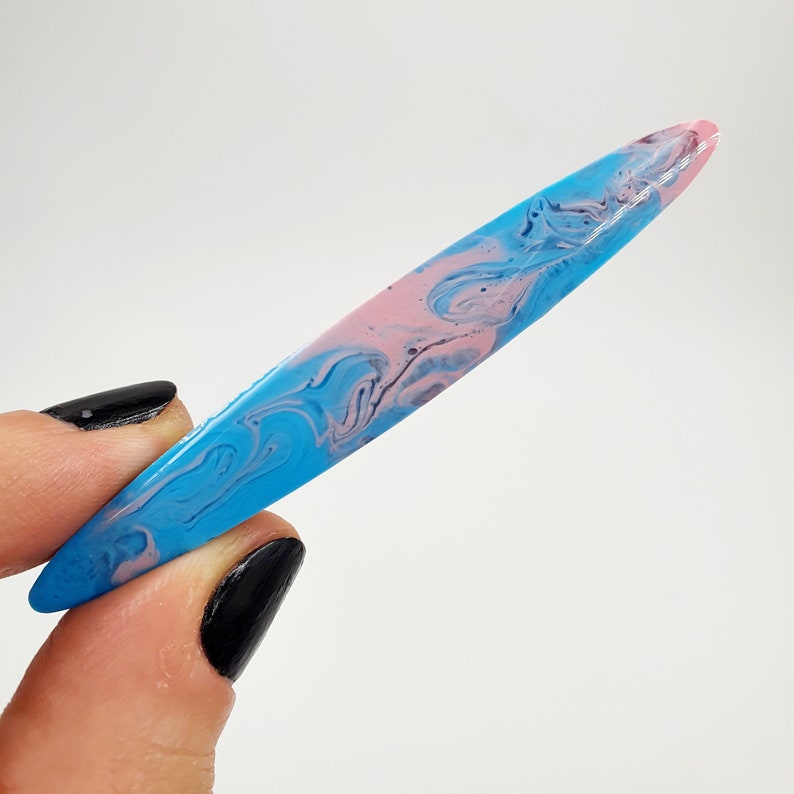 Op de afbeelding: Een lang, dun, blauw en roze marmerachtig, decoratief harsobject. Het object heeft een gladde, glanzende afwerking.