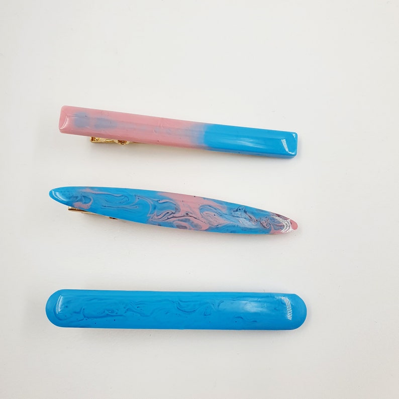 Op de afbeelding: Drie haarclips met een marmerpatroon. De bovenste clip is roze en blauw, de middelste clip is blauw en roze en de onderste clip is blauw.