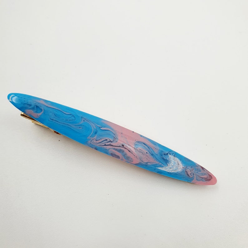 Op de afbeelding: Een blauwe en roze marmeren haarspeld met een gouden metalen sluiting.