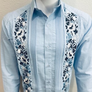 May include: A light blue long-sleeved shirt with white and blue floral embroidery on the front.