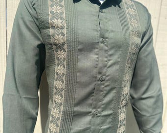 May include: A long-sleeved, button-down shirt in a muted green hue. The shirt features intricate embroidered panels with a floral design in a lighter shade of green. The shirt has a classic collar and buttoned cuffs, suitable for casual or semi-formal wear.