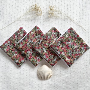May include: Five reusable makeup remover pads with a floral print in shades of red, green, and white. The pads are arranged in a diamond shape with a white shell in the center.