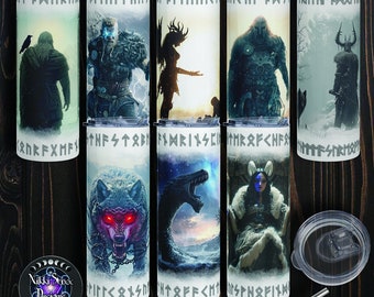 Könnte beinhalten: Satz von acht Edelstahl-Bechern mit verschiedenen Designs, die Figuren und Symbole der nordischen Mythologie zeigen. Die Becher sind weiß mit schwarzen und blauen Akzenten. Jeder Becher hat ein anderes Design, darunter ein Wolf, ein Drache, ein Krieger und eine Walküre. Die Becher sind perfekt, um Getränke kalt oder warm zu halten.