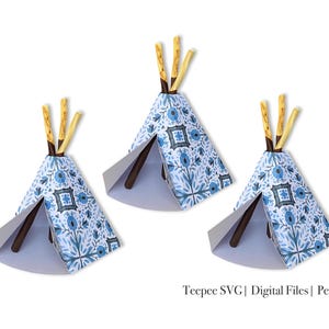 Puede incluir: Tres tipis de papel azul y blanco con palos marrones para postes. Los tipis son un proyecto de manualidades.