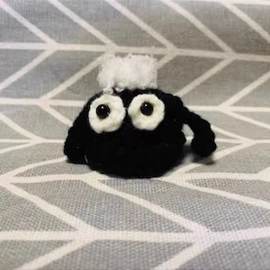 Könnte beinhalten: Ein kleines schwarzes Amigurumi-Spielzeug aus Häkelgarn mit weißen Augen aus Wolle und einem weißen, flauschigen Büschel auf dem Kopf.