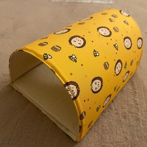 May include: A yellow fabric tunnel with a repeating pattern of cartoon hedgehogs and honeycombs. The tunnel is curved and has a white interior.