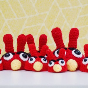 May include: A group of seven red crocheted Angry Birds characters. The characters are all different sizes and have different expressions on their faces.