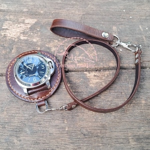 Pode incluir: Uma pulseira de relógio de couro marrom com um mostrador de relógio prateado. O mostrador do relógio tem ponteiros pretos e um mostrador preto com marcas brancas. O mostrador do relógio diz "Luminor Marina" e "Panerai".