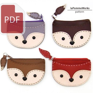 Könnte beinhalten: Vier fuchsförmige Münzbörsen in verschiedenen Farben: Grau, Braun, Dunkelbraun und Rot. Jede Börse hat ein cremefarbenes Gesicht, schwarze Augen und einen Reißverschluss. Die Börsen sind aus Leder gefertigt und haben einen blattförmigen Reißverschlussanhänger. Der Text "laPommeWorks pattern" ist sichtbar.