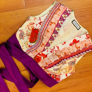 May include: A white, orange, and purple floral print top with a purple satin sash. The top has a V-neck and is sleeveless. The label "KALPANA SINGH" is visible on the top.