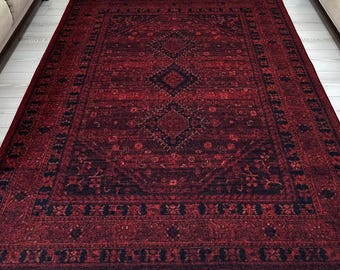 May include: A rectangular, red area rug with a dark, intricate pattern dominates the room. The rug is centered in front of a neutral-toned armchair and two matching sofas. The room is decorated with floral accents and light-colored curtains.