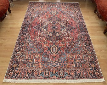 Puede incluir: Una alfombra roja, negra y azul con un patrón y flecos blancos. La alfombra está colocada sobre un suelo de madera en un salón con dos sillones rojos y una mesa pequeña en el fondo.