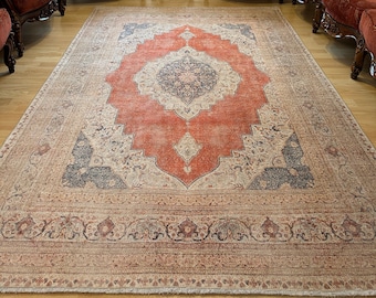 May include: A vintage-style rug with a faded orange and cream color scheme. The rug has a central medallion with intricate floral designs and a border with repeating patterns. The rug is laid out on a hardwood floor in a room with antique furniture.