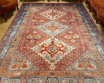 May include: A large, intricately patterned rug with a red, blue, and cream color scheme. The rug has a central medallion with floral and geometric designs. The rug is surrounded by a border with a repeating pattern.