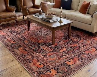 May include: A large rectangular area rug featuring a dark red and black intricate pattern with stylized animal and floral motifs. The rug is positioned on a light wood floor in a room containing a beige sofa, two brown leather chairs, and a wooden coffee table.