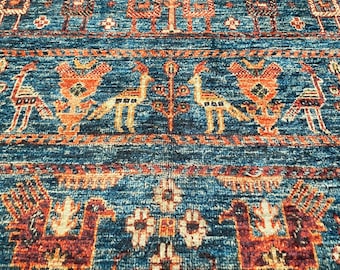 Könnte beinhalten: Nahaufnahme eines blau-rostfarbenen Teppichs mit detailliertem Muster. Der Teppich zeigt sich wiederholende geometrische Designs und stilisierte Tierfiguren. Die Farbpalette umfasst Blau-, Orange- und Brauntöne und erzeugt eine warme Ästhetik.