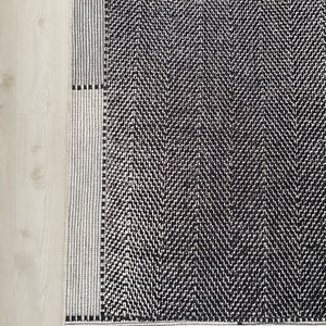 Pu&ograve; includere: Tappeto a chevron bianco e nero con bordo bianco. Il tappeto ha un design geometrico con una texture sottile.