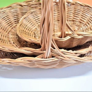 Pu&ograve; includere: Tre cesti in vimini intrecciato con manici, annidati l'uno nell'altro. I cesti sono di forma ovale e in vimini marrone naturale.