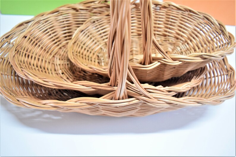 Pu&ograve; includere: Tre cesti in vimini intrecciato con manici, annidati l'uno nell'altro. I cesti sono di forma ovale e in vimini marrone naturale.