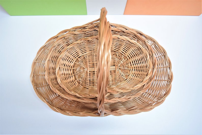 Pu&ograve; includere: Un set di tre cesti in vimini intrecciati con un manico. I cesti sono di forma ovale e sono annidati l'uno dentro l'altro.