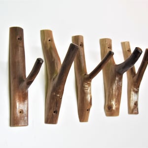 May include: Set of six wooden wall hooks, each shaped like a branch with a natural brown finish. The hooks are mounted on a white wall.
