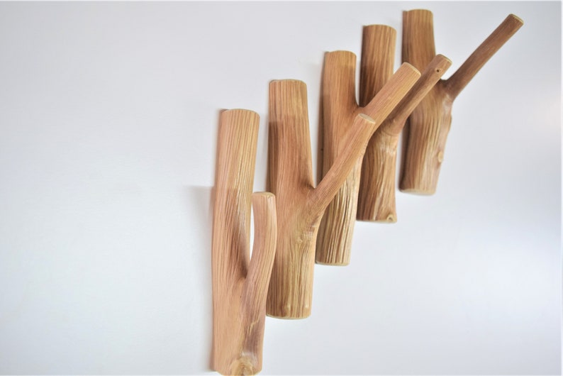 May include: A set of six wooden wall hooks shaped like branches. The hooks are arranged in a staggered pattern, with the longest hook at the top and the shortest hook at the bottom. The hooks are a natural wood color and have a rustic look.