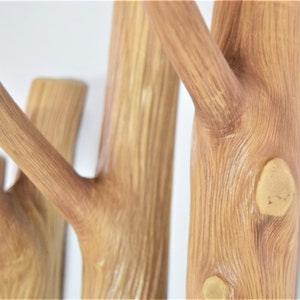 May include: A wooden wall-mounted coat rack with multiple branches, resembling a tree. The branches are finished in a light brown color and have a natural wood grain texture.