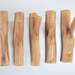 May include: Five wooden hooks made from natural branches, each with a unique shape and grain pattern. The hooks are ideal for hanging coats, hats, or other items in a rustic or farmhouse style.