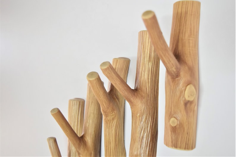 May include: A set of wooden wall hooks shaped like tree branches. The hooks are arranged in a staggered pattern, with the largest hook at the top and the smallest hook at the bottom. The hooks are a light brown color and have a natural wood grain.