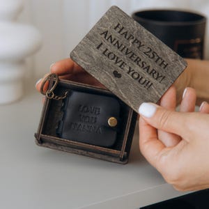 May include: A small wooden box containing a black leather keychain. The box lid is engraved with the message "Happy 25th Anniversary! I Love You!!". The keychain has the inscription "Love You Hanna" on it.