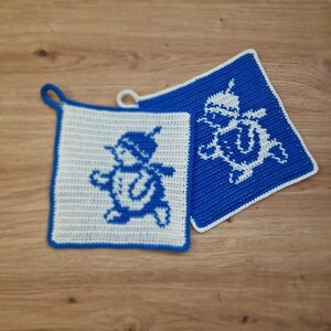 May include: Two square, crocheted potholders. One is white with a blue border and a blue cartoon character. The other is blue with a white cartoon character and a white border. Both have a loop for hanging.