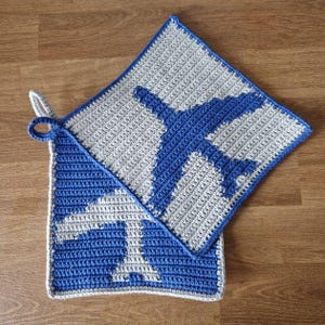 Könnte beinhalten: Zwei gehäkelte Topflappen mit einem blauen Flugzeugdesign. Ein Topflappen ist grau mit einem blauen Flugzeug, der andere ist blau mit einem grauen Flugzeug.