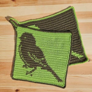 May include: Two handmade crochet potholders. One is lime green with a brown bird silhouette. The other is brown with a lime green border. Both are square with a loop for hanging. The potholders are on a wooden surface.