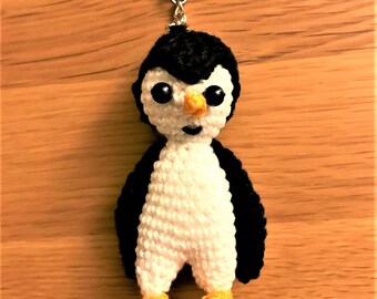 May include: A crocheted penguin keychain with black wings, a white body, and yellow feet. The penguin has black eyes and an orange beak.