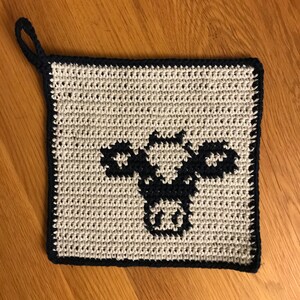 May include: A white crocheted pot holder with a black crocheted cow design.