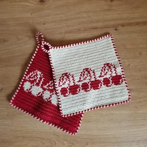 Puede incluir: Dos agarraderas de ganchillo hechas a mano. Una es roja con un diseño de cerezas blancas, la otra es blanca con un diseño de cerezas rojas. Ambas tienen un borde rojo y blanco y un lazo para colgar. Las agarraderas son cuadradas.