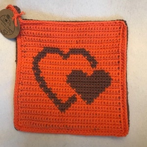 Könnte beinhalten: Orangener gehäkelter Topflappen mit einem braunen Herzdesign.