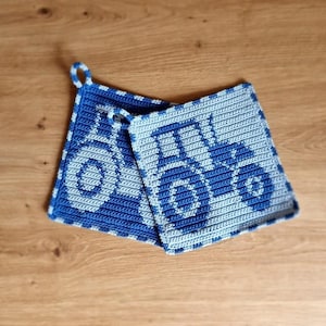 May include: Two blue and light blue crochet potholders with a tractor design. The potholders are square-shaped and feature a loop for hanging. The tractor design is visible on both potholders, with a blue border.