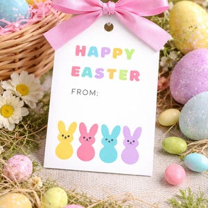 May include: A white gift tag with a pink bow, featuring the text "HAPPY EASTER" in colorful letters and four bunny illustrations. The tag is surrounded by decorated Easter eggs in a basket and on a bed of grass.