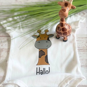 May include: White baby onesie with a brown and gray giraffe illustration and the word "Hallo!" printed on the front.