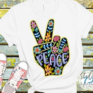 May include: White t-shirt with a peace sign design featuring colorful flowers and the word "PEACE" in purple lettering.
