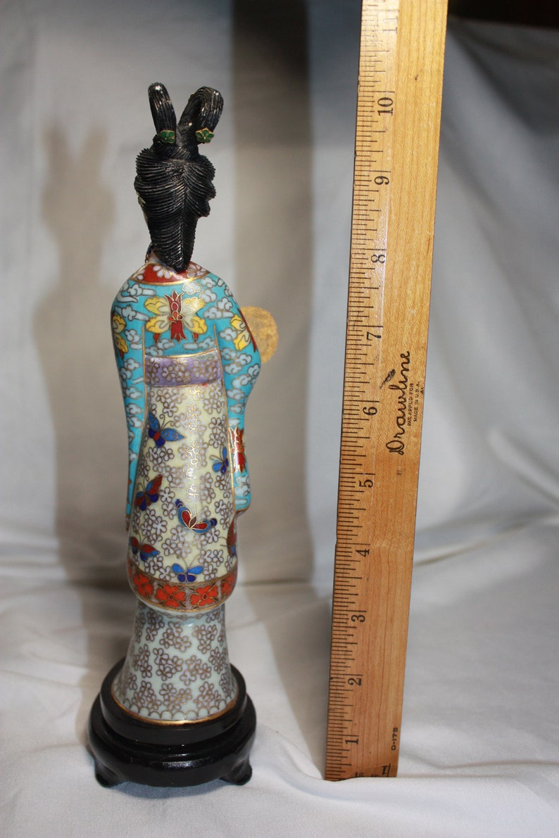 May include: A cloisonn&eacute; figurine of a woman in a blue, white, and gold robe with a black hairpiece and a fan. The figurine is standing on a black base.
