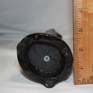 May include: The bottom of a black ceramic figurine with a screw in the center. The figurine is about 6 inches tall.