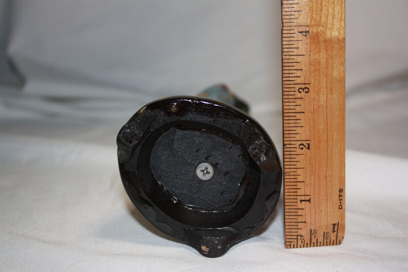 May include: The bottom of a black ceramic figurine with a screw in the center. The figurine is about 6 inches tall.