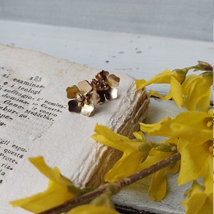 Op de afbeelding: Een paar gouden oorringen in de vorm van een bloem met kleine gouden kralen in het midden van elke bloem.