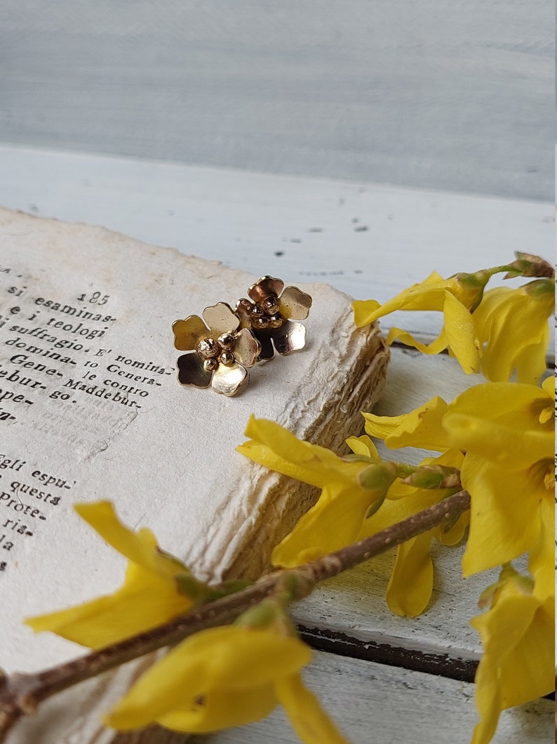 Op de afbeelding: Een paar gouden oorringen in de vorm van een bloem met kleine gouden kralen in het midden van elke bloem.
