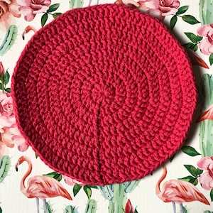 Op de afbeelding: Een ronde, felrode gehaakte onderzetter. De onderzetter is gemaakt van dik garen en heeft een textuur.
