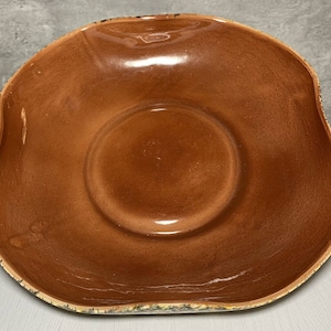 May include: A large, brown ceramic serving bowl with a wavy rim and a glossy finish. The bowl has a slightly raised center.