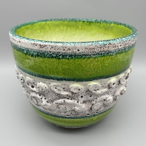 May include: A ceramic bowl with a textured, layered design. The interior is bright green, with a wide band of green around the middle. The bottom half features a white, textured pattern. The rim is white with black speckles.